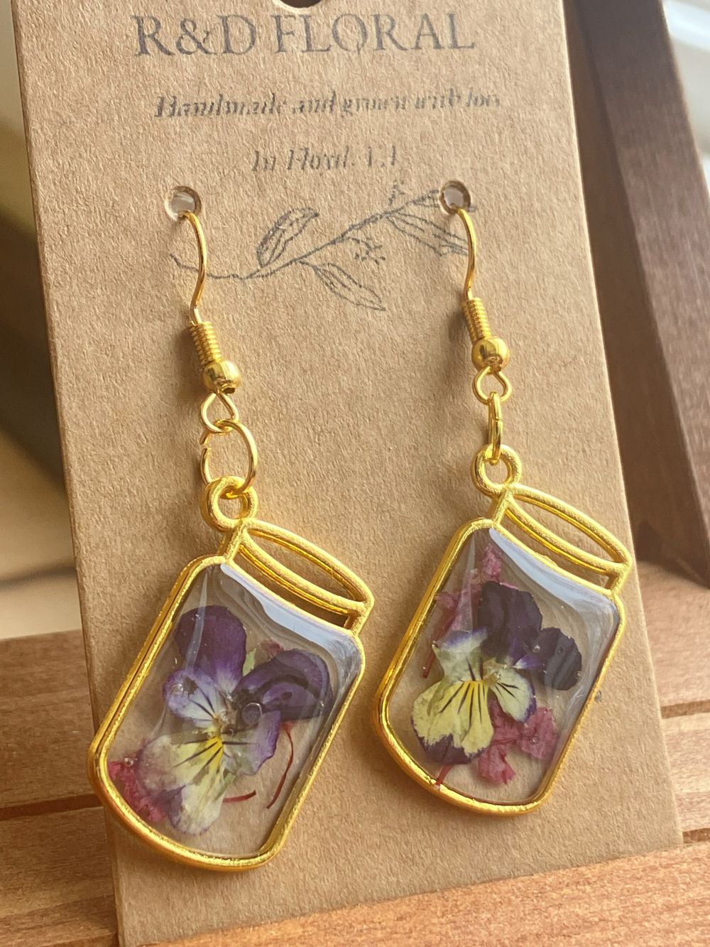 Metal mason jar–shaped earrings encasing real Viola flowers in resin handmade by R & D Floral.